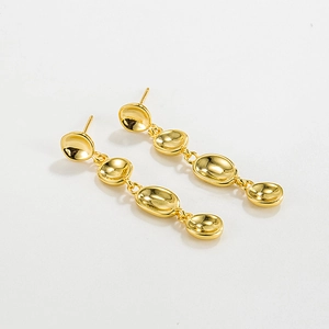 Detailed view of long gold tassel earrings with four concave oval metal pieces on white surface