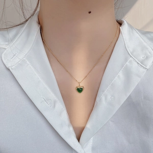 Close-up of heart-shaped green gemstone pendant with gold bead chain on a white shirt