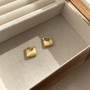 Macro detail of S925 sterling silver handbag-shaped earrings with matte gold finish