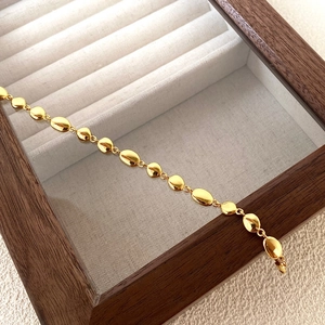 Macro view of polished gold bean-shaped chain bracelet on a walnut jewelry box