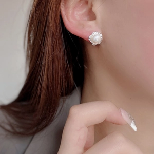 Close-up of irregular silver metal stud earrings with round white pearl on the ear