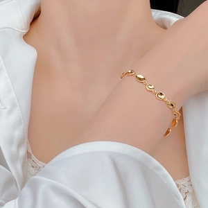 Macro detail of gold-plated textured pea bead bracelet on a model's wrist wearing lace