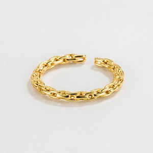 Détail de la bague réglable en forme de maille dorée sur un fond gris neutre