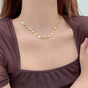 Dettaglio della collana a chicchi d'oro irregolari indossata su un maglione marrone caldo