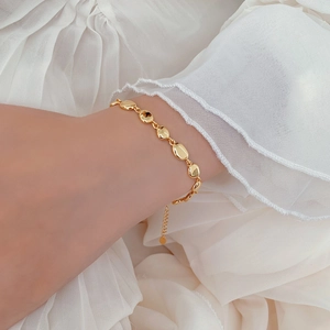 Detailed view of an adjustable gold pea link bracelet worn on a female wrist over silk fabric