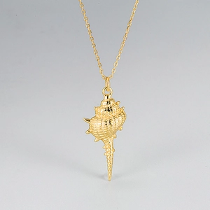 Macro shot of detailed golden murex shell pendant on a fine minimalist link chain