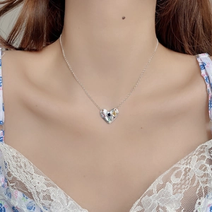 Détail d'un pendentif cœur avec zircons colorés porté par un mannequin en dentelle blanche