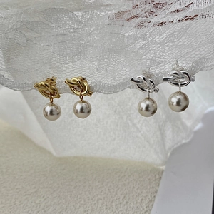 Detailed close-up of knotted metal pearl earrings in gold and silver on white lace