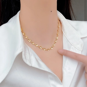 Dettaglio di una collana dorata minimalista con maglie concave irregolari sulla modella
