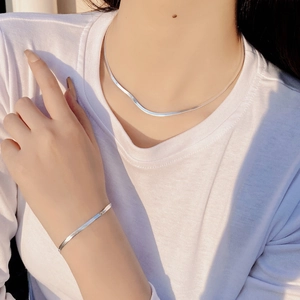 Detail of minimalist S925 sterling silver flat snake chain set worn by a model in sunlight