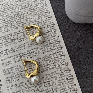 Macro shot of minimalist gold S925 silver pearl earrings resting on vintage book pages