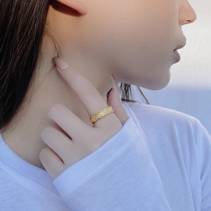 Detailed view of an 18K gold ring with intricate floral engraving on a model's hand