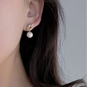 Close-up of elegant gold knot pearl earrings worn by a model in a natural setting