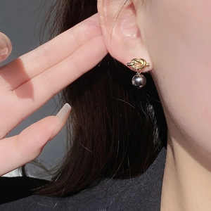 Close-up of knot-shaped gold stud earring with dark grey pearl on model's ear