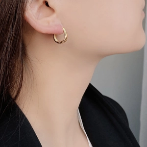 Close-up of a model wearing a gold twisted C-shape hoop earring with a textured wheat pattern