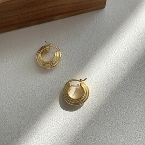 Dettaglio di orecchini a cerchio a tripla spirale in argento S925 con finitura dorata