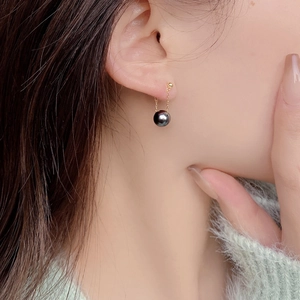 Detailed view of grey round pearl drop earring with gold chain on ear