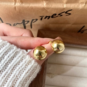 Close-up of polished gold spherical earrings held by hand with a soft knit background