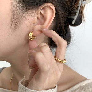 Dettaglio di orecchini dorati a cerchi multipli e anello intrecciato sulla modella