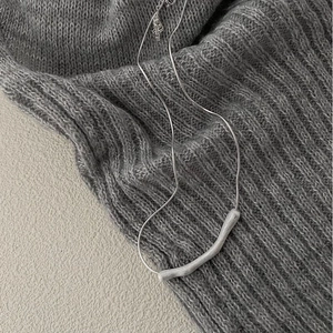 Detail of minimalist 925 silver bar necklace draped on a textured grey knit sweater