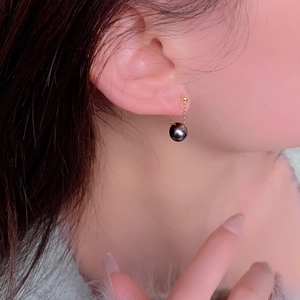 Detailed side view of a black round pearl drop earring with a delicate gold chain link