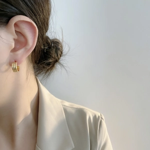 Détail de boucles d'oreilles créoles dorées à trois couches portées par un mannequin