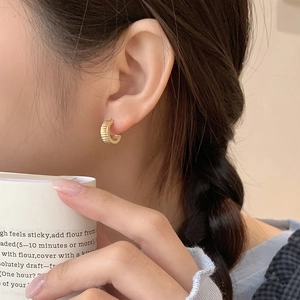 Close-up of a gold pleated gear hoop earring on a model for minimalist industrial style