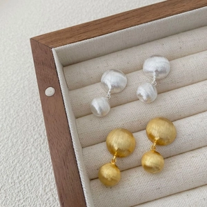 Brushed metal double ball drop earrings in silver and gold on a jewelry box display
