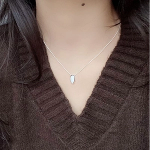 Gros plan du collier goutte en argent S925 avec incrustation blanche sur un pull en V