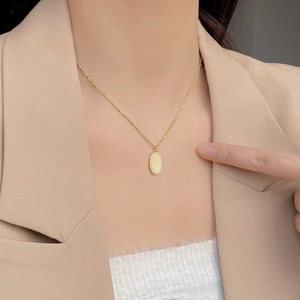 Close-up of minimalist gold oval pendant necklace on model with refined matte finish