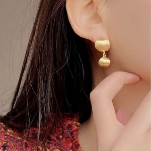 Golden double ball drop earrings with brushed metal texture worn on a female model