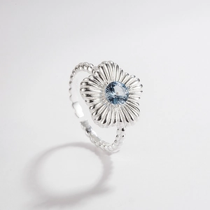 Close-up of a silver flower ring featuring a light blue zircon and beaded texture band