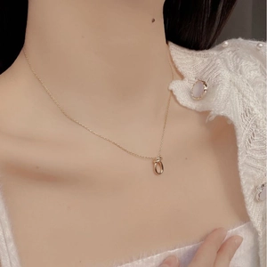 Detail of a minimalist gold knot pendant necklace worn over a white knitted sweater