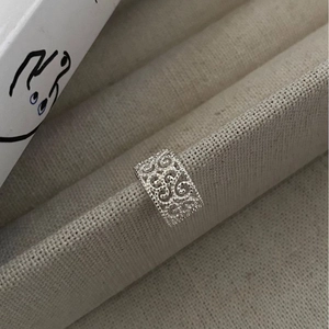 Hollow-out sterling silver ear cuff with traditional floral patterns on beige display