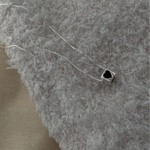 Detailed close-up of a silver cube pendant with a black heart on a delicate link chain