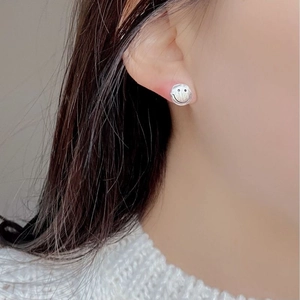 Close-up of minimalist silver smiley face stud earring worn on a female model's earlobe