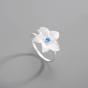 Macro detail of silver hibiscus flower ring featuring a sparkling blue gemstone center