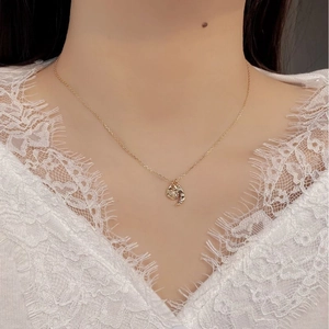 Close-up of a golden crescent moon pendant necklace with a white pearl on a model's neck