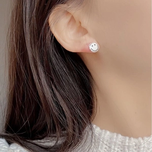 Macro detail of minimalist 925 silver smiley face stud earring worn by a model