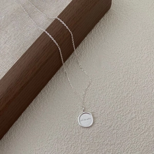 Macro shot of matte silver round pendant with all is well engraving on wooden block