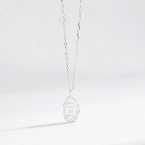Irregular matte silver pendant necklace with live and let live engraving on white background