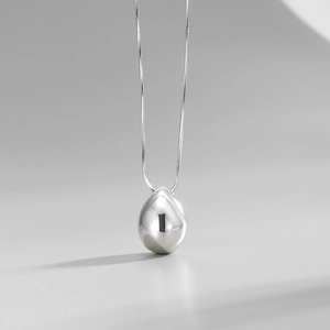 Détail macro du pendentif goutte d'argent poli sur une fine chaîne serpent élégante