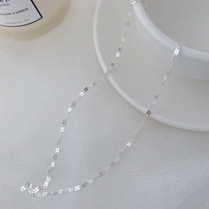 Close-up of S925 sterling silver flat clover link chain on elegant white fabric