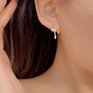 Detail of elegant gold ribbon bow earring with sparkling cubic zirconia on female ear