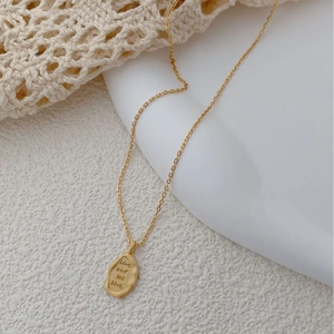 Detail of matte gold irregular pendant engraved with Live and let live on a fine chain