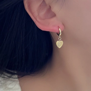 Close-up of a gold heart charm earring with frosted texture and rope edge on a model