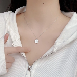 Close-up of minimalist silver round pendant necklace worn over a white hoodie
