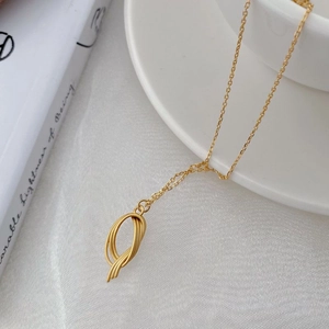 Macro detail of a twisted circular matte gold pendant on a minimalist silver chain necklace