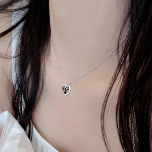 Detail of S925 silver heart necklace with black enamel and red cherry motif on a model