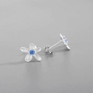 Macro detail of silver flower stud earrings with matte petals and blue zircon center
